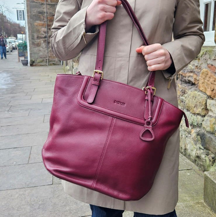 Person holding a maroon handbag with a visible brand logo on a sidewalk.