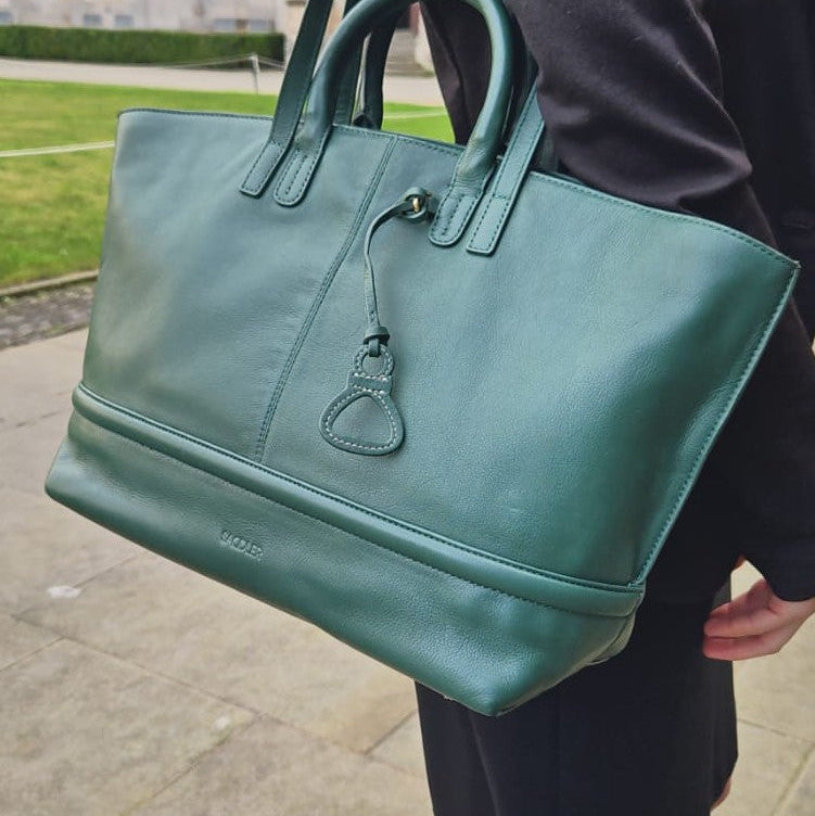 Green handbag held by a person outdoors on a stone path.