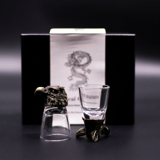 Two shot glasses with decorative stands in front of a branded box on a dark background