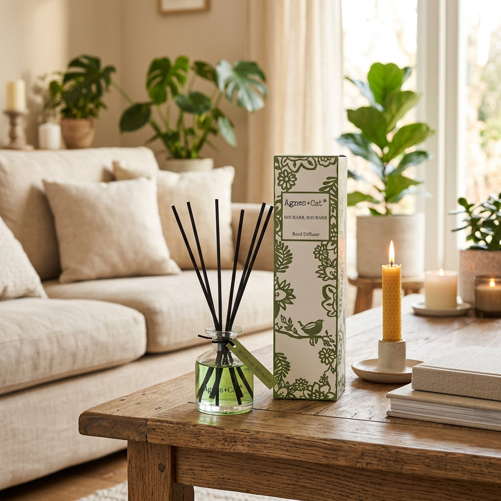 A reed diffuser bottle with green liquid and black reeds, shown next to its white and green patterned box on a plain white background.
